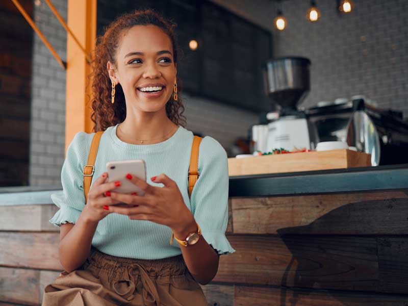 FollowMyMoney Aktien, ETFs, Optionsscheine erfolgreiche und glückliche Frau vor einem Kaffeehaus